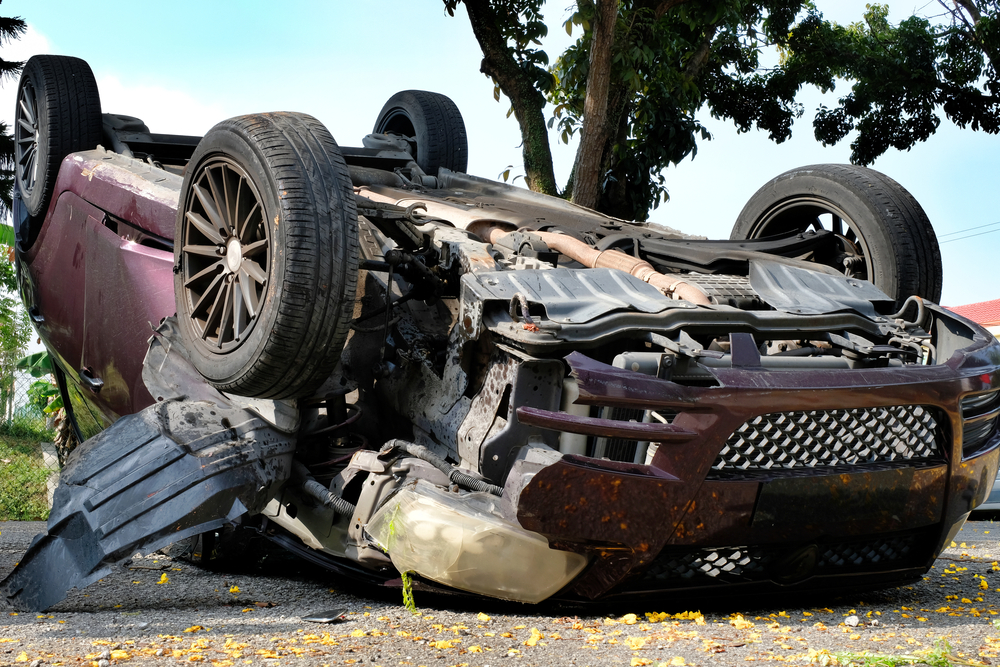 An overturn car lying upside down on a street after an accident suffering heavy damage